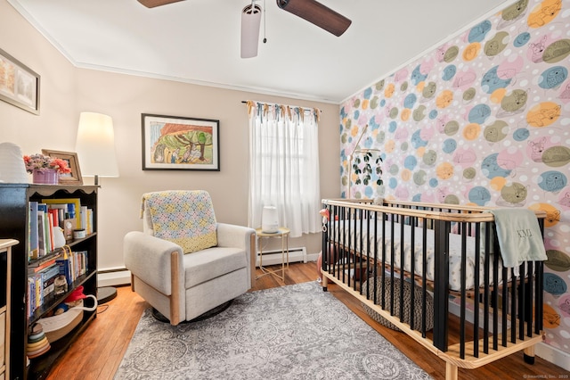 bedroom featuring hardwood / wood-style floors, ceiling fan, a baseboard heating unit, and a nursery area