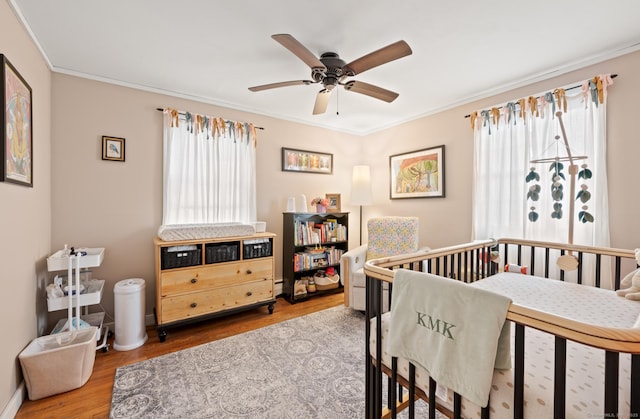 bedroom with a crib, wood-type flooring, ceiling fan, and crown molding