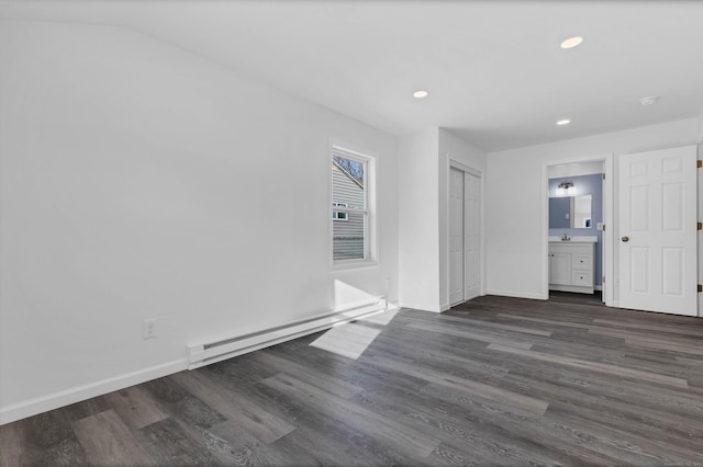 unfurnished bedroom featuring ensuite bathroom, a closet, a baseboard radiator, and dark hardwood / wood-style floors