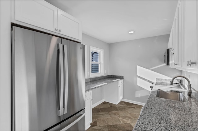 kitchen with white cabinetry, dark stone countertops, stainless steel fridge, and sink