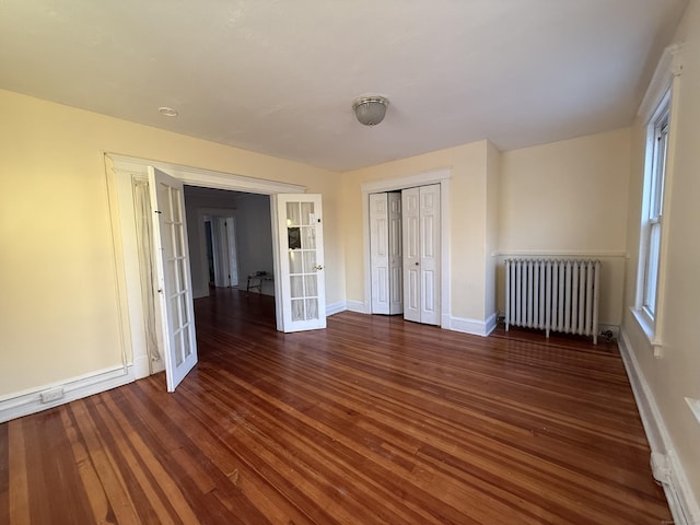 unfurnished bedroom with dark hardwood / wood-style flooring, radiator heating unit, french doors, and a closet