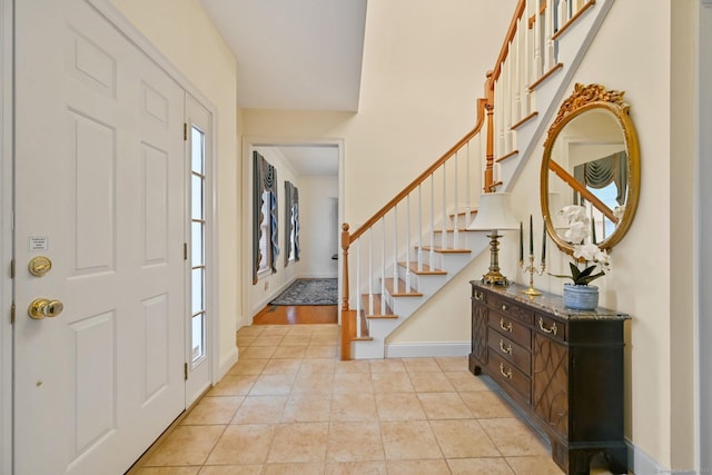 foyer entrance with light tile patterned floors, stairway, and baseboards