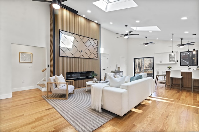 living room featuring a skylight, a fireplace, light hardwood / wood-style floors, and a high ceiling