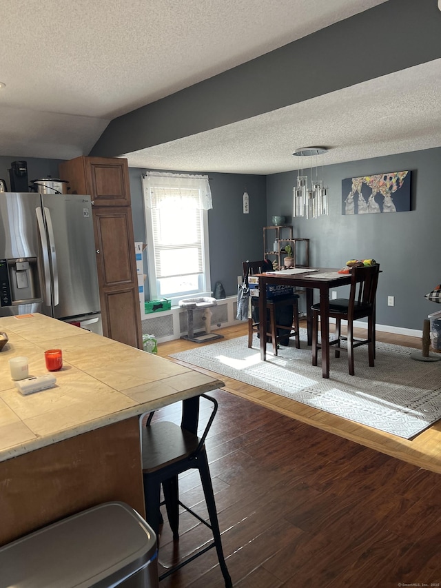 kitchen with hanging light fixtures, dark hardwood / wood-style floors, tile countertops, stainless steel fridge, and vaulted ceiling