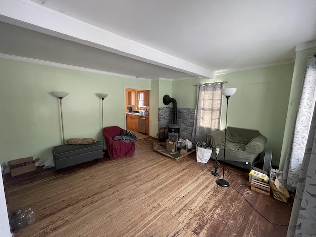 living room with wood-type flooring, ornamental molding, beamed ceiling, and a wood stove