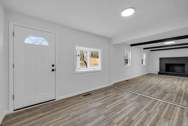 entrance foyer with a brick fireplace, plenty of natural light, light hardwood / wood-style floors, and beamed ceiling