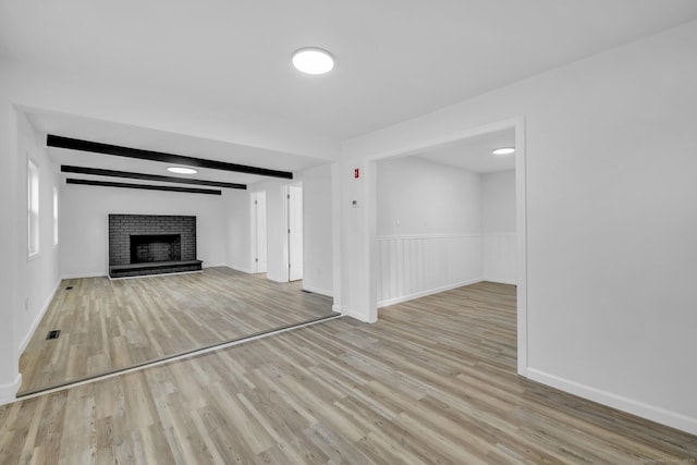 unfurnished living room with beamed ceiling, light wood-type flooring, and a fireplace