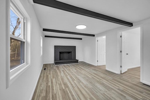 unfurnished living room featuring beamed ceiling, a brick fireplace, and light hardwood / wood-style flooring