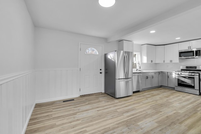 kitchen with appliances with stainless steel finishes, sink, light wood-type flooring, and white cabinets