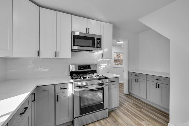 kitchen with gray cabinets, white cabinets, light stone counters, stainless steel appliances, and light wood-type flooring