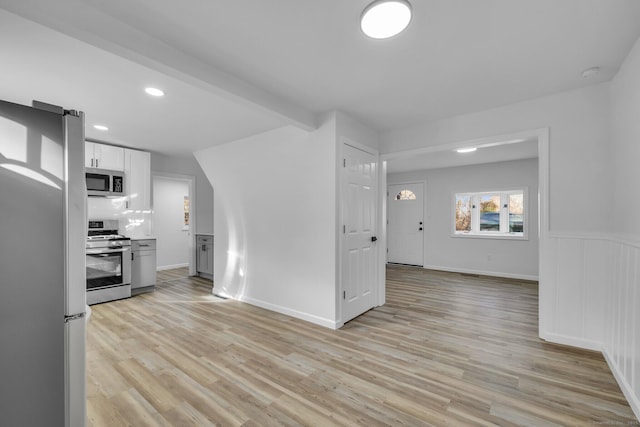 kitchen featuring appliances with stainless steel finishes, white cabinetry, decorative backsplash, light hardwood / wood-style floors, and beam ceiling