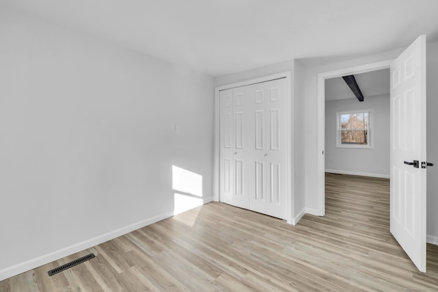 unfurnished bedroom featuring beamed ceiling, light hardwood / wood-style floors, and a closet