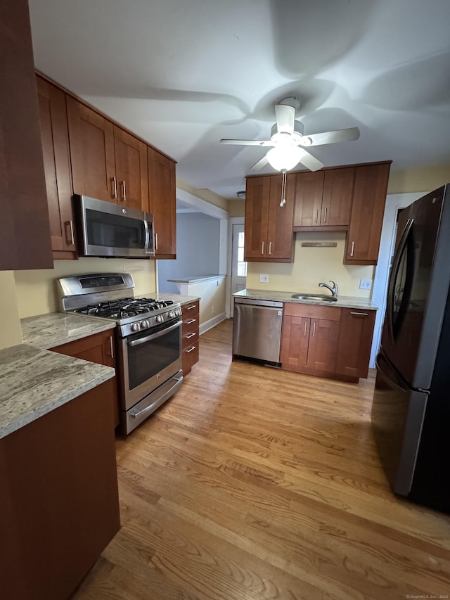 kitchen featuring light stone countertops, ceiling fan, sink, appliances with stainless steel finishes, and light wood-type flooring