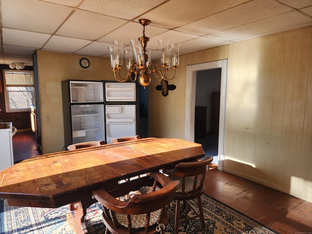 dining area featuring wood walls, a chandelier, and a drop ceiling