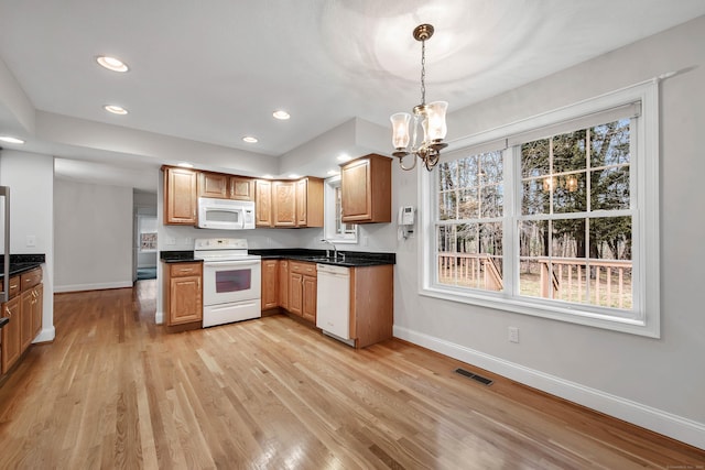 kitchen with white appliances, hanging light fixtures, a chandelier, light hardwood / wood-style flooring, and sink