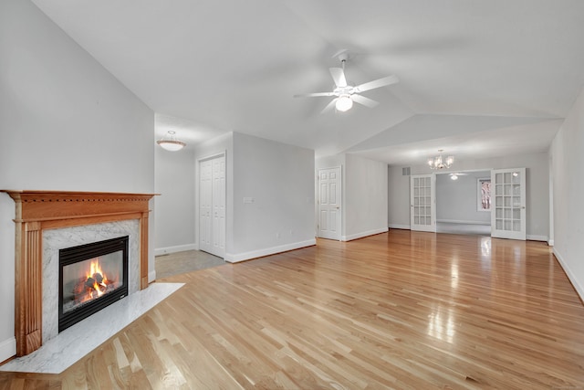 unfurnished living room featuring light wood-type flooring, lofted ceiling, french doors, a high end fireplace, and ceiling fan with notable chandelier