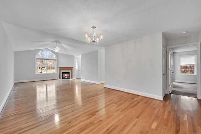 unfurnished living room with light wood-type flooring, lofted ceiling, ceiling fan with notable chandelier, and plenty of natural light