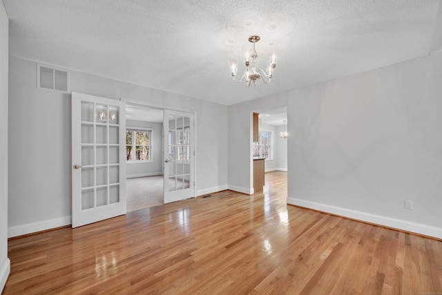 interior space with a textured ceiling, hardwood / wood-style floors, french doors, and an inviting chandelier