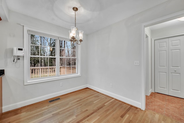 unfurnished dining area with a wealth of natural light, light hardwood / wood-style flooring, and a notable chandelier