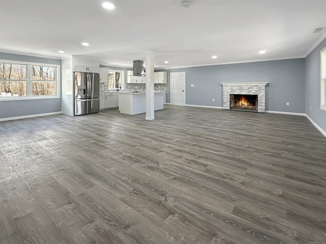 unfurnished living room featuring crown molding, a stone fireplace, dark wood-type flooring, and sink