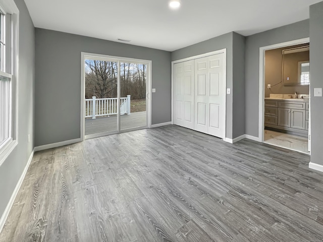 unfurnished bedroom featuring sink, hardwood / wood-style flooring, connected bathroom, access to outside, and a closet