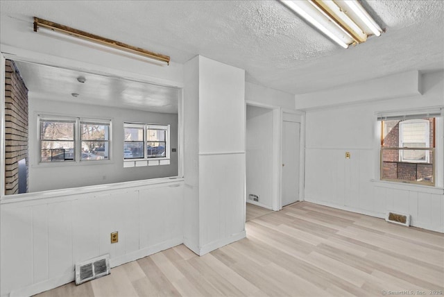 spare room with wooden walls, a textured ceiling, and light wood-type flooring