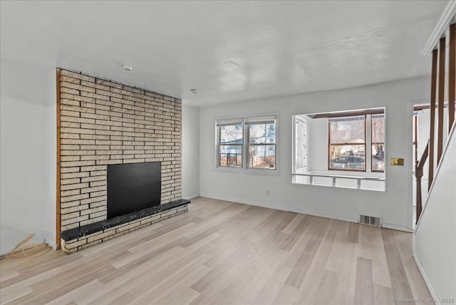 unfurnished living room featuring light hardwood / wood-style floors and a brick fireplace