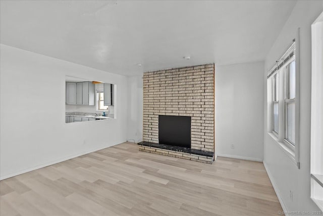 unfurnished living room featuring light hardwood / wood-style flooring and a brick fireplace