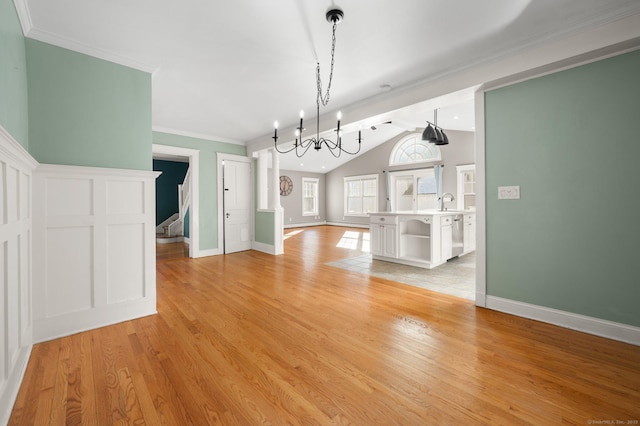 unfurnished dining area with lofted ceiling, an inviting chandelier, sink, light wood-type flooring, and ornamental molding