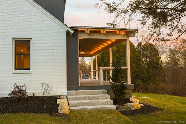 exterior entry at dusk with a lawn and covered porch