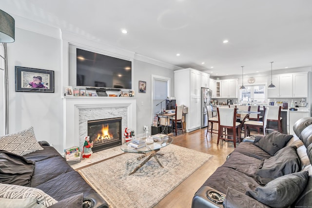 living room featuring a high end fireplace, light hardwood / wood-style floors, and ornamental molding