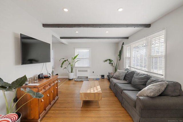 living room featuring beamed ceiling, radiator heating unit, light hardwood / wood-style floors, and a healthy amount of sunlight