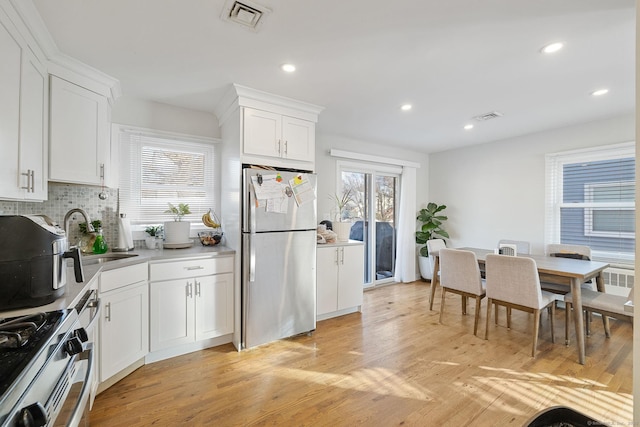 kitchen featuring backsplash, sink, light hardwood / wood-style flooring, white cabinets, and stainless steel refrigerator