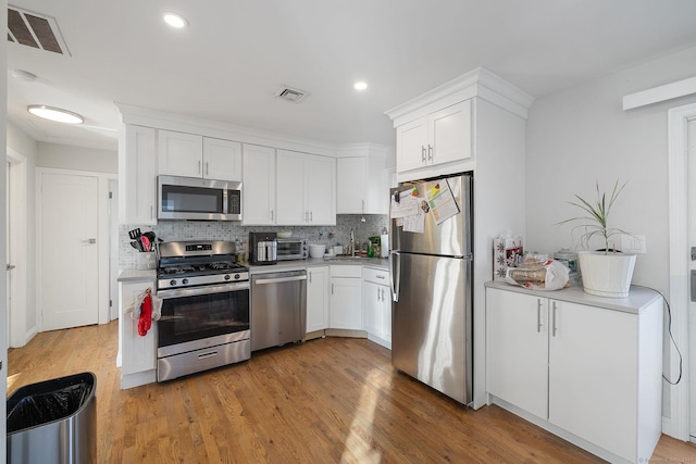 kitchen with tasteful backsplash, white cabinetry, hardwood / wood-style floors, and stainless steel appliances