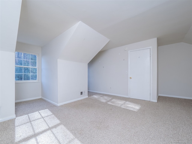 additional living space featuring light colored carpet and vaulted ceiling