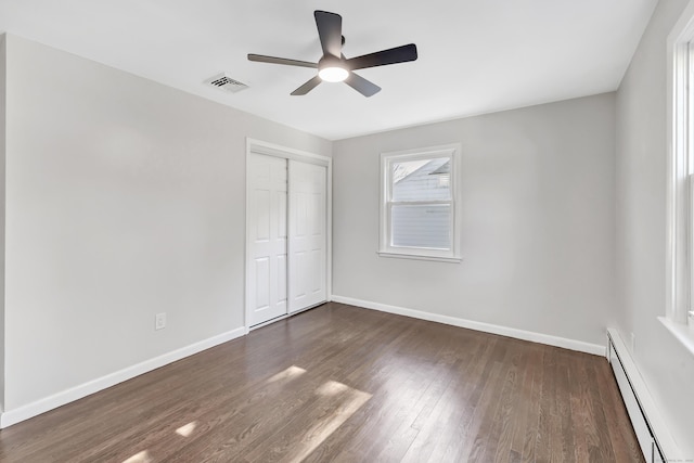 unfurnished bedroom featuring baseboard heating, ceiling fan, a closet, and dark hardwood / wood-style floors