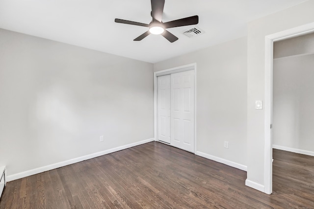 unfurnished bedroom with ceiling fan, a baseboard heating unit, dark hardwood / wood-style flooring, and a closet