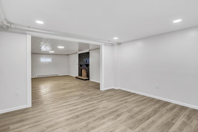 basement with light wood-type flooring, a brick fireplace, and baseboard heating