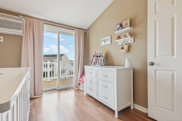 bedroom with access to outside, vaulted ceiling, a wall mounted AC, and light hardwood / wood-style floors