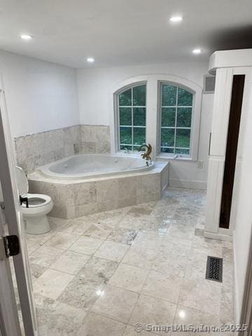 bathroom with a relaxing tiled tub and toilet