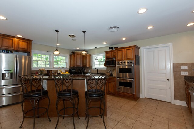 kitchen featuring light tile patterned floors, a center island, stainless steel appliances, and dark stone counters