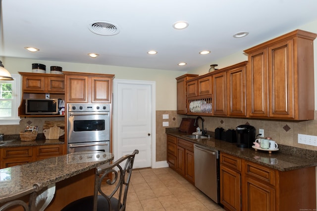 kitchen with a kitchen breakfast bar, dark stone countertops, sink, and appliances with stainless steel finishes