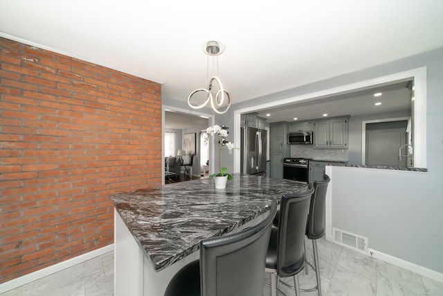 kitchen featuring decorative backsplash, appliances with stainless steel finishes, gray cabinetry, a breakfast bar, and decorative light fixtures