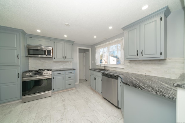 kitchen with sink, dark stone countertops, a textured ceiling, tasteful backsplash, and stainless steel appliances