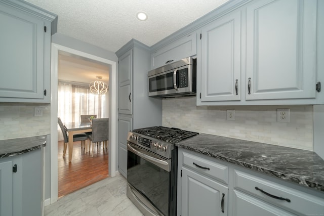 kitchen with backsplash, dark stone counters, a textured ceiling, stainless steel appliances, and an inviting chandelier