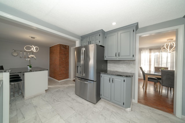 kitchen featuring stainless steel refrigerator with ice dispenser, backsplash, dark stone countertops, a chandelier, and gray cabinets