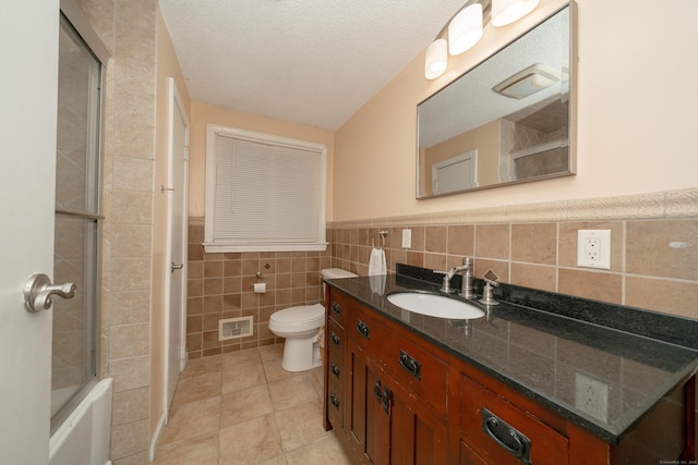 full bathroom featuring tile patterned flooring, a textured ceiling, toilet, vanity, and tile walls