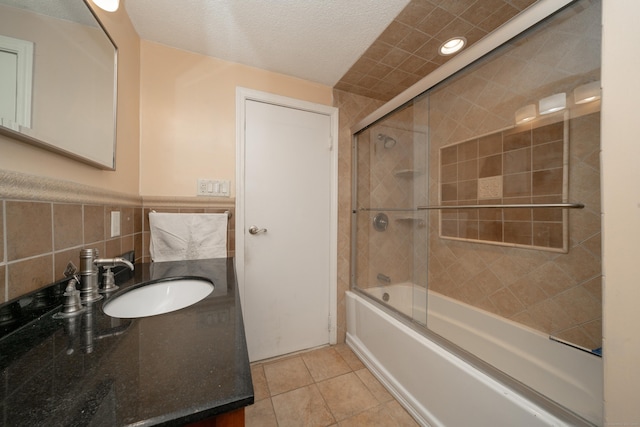 bathroom with combined bath / shower with glass door, tile patterned floors, a textured ceiling, vanity, and tile walls