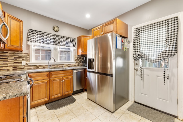 kitchen with sink, stainless steel appliances, dark stone counters, decorative backsplash, and light tile patterned flooring