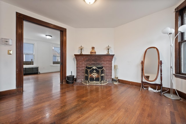 living room featuring dark hardwood / wood-style flooring, radiator heating unit, and a brick fireplace